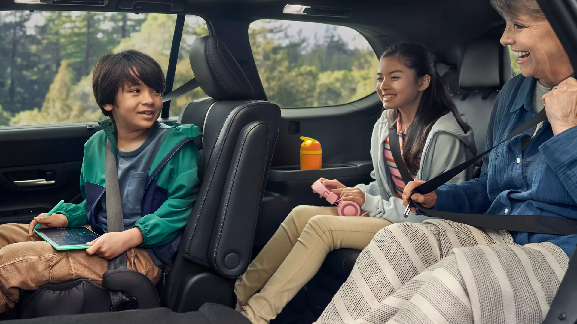 Inside a Toyota Grand Highlander, two children in the second row and a grandmother in the third row, the sliding door open to a forest.