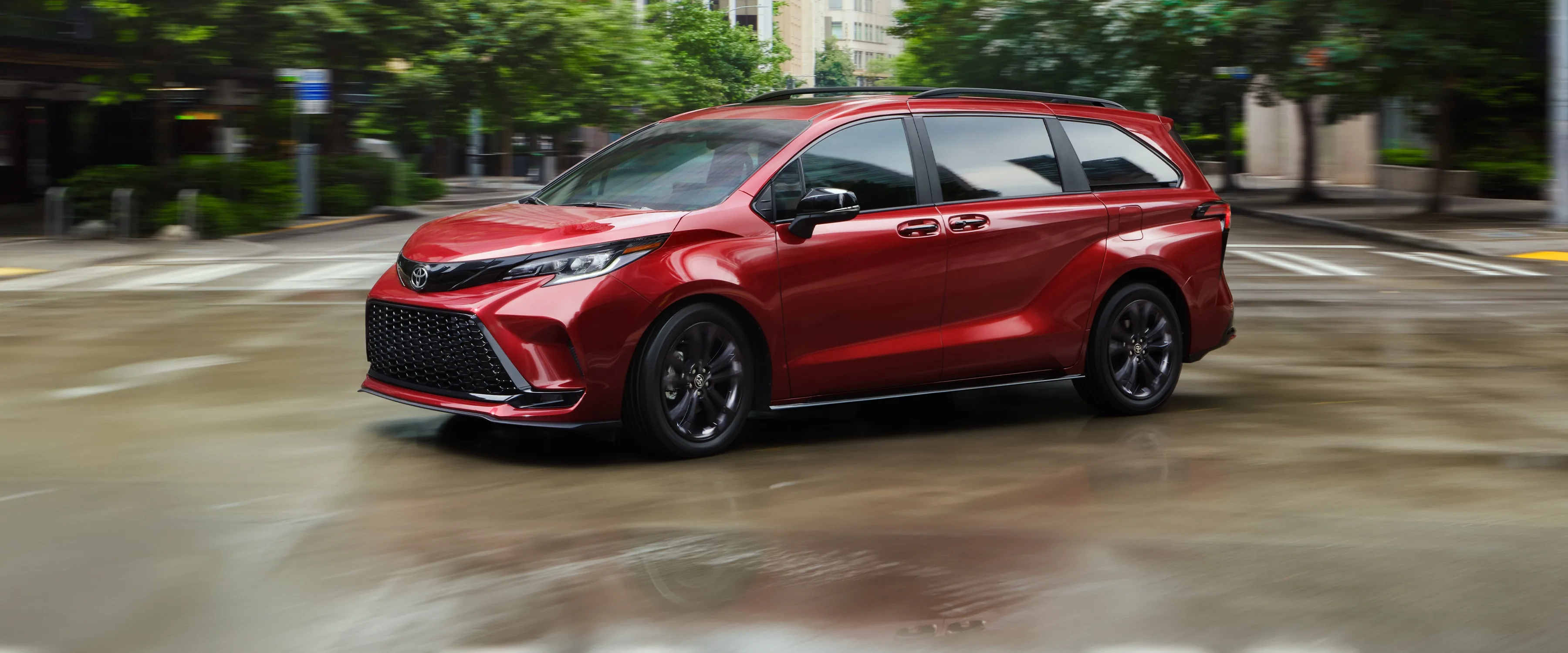 A red Toyota Sienna minivan crossing a wet city street
